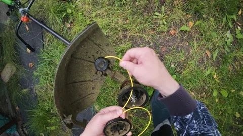 Man replacing trimmer line in powerful electric grass trimmer first person .. Stock Footage 340143545