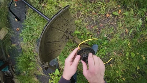 Man replacing trimmer line in powerful electric grass trimmer first person .. Stock Footage 340143546