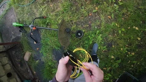 Man replacing trimmer line in powerful electric grass trimmer first person .. Stock Footage 340143629