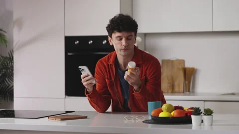 Man researching information about pills on phone in kitchen, reading side effect Stock Footage 341016644