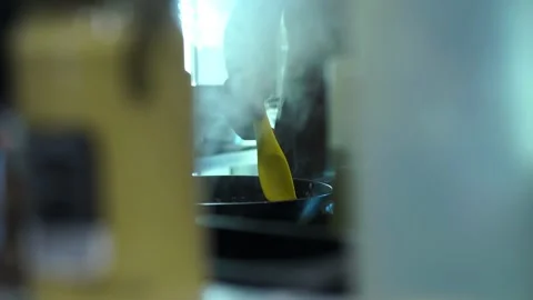 A man in a restaurant kitchen stirring a dish in a frying pan, steam goes Stock Footage 141246200