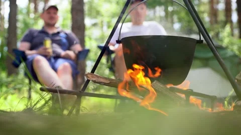 Man resting and cooking in pot on fire. Tourist trip. Camping Stock Footage 219992610