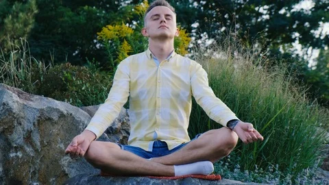 Man is resting and meditating while sitting on larger stones Stock Footage 119418346