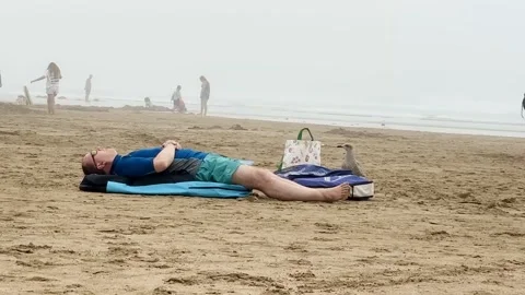 Man Resting on Blue Beach Mat With Personal Belongings at Woolacombe Beach Devon Vídeo Stock 346221026