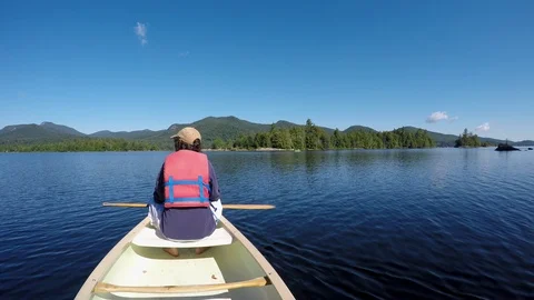 Man resting in a canoe on a lake as the clouds overhead reveal full sunlight Stock Footage 90088913