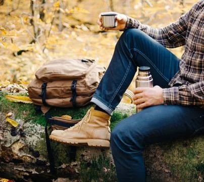 Man resting on fallen tree trunk with thermos. Stock Photos