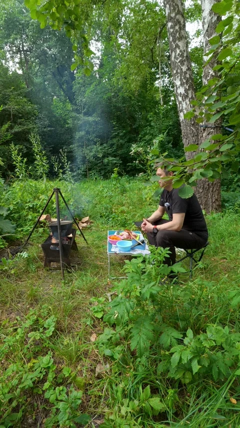 Man resting on folding chair while cooking food in campfire cauldron outdoo.. Vídeo Stock 347606243