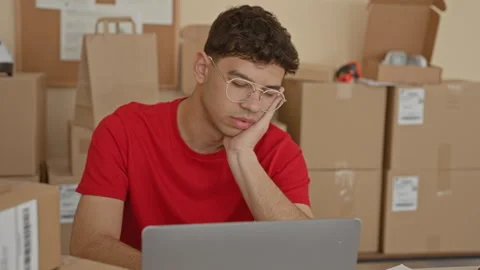 Man resting head on hand while using laptop amid stacked boxes in a buildin.. Stock Footage 337376449
