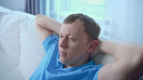 A man is resting with his hands behind his head, sitting on the couch Stock Footage 216749513