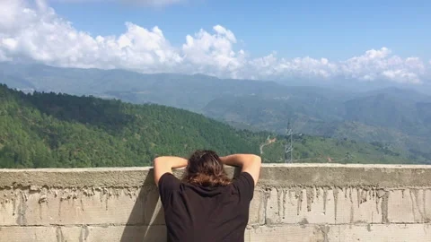 A man resting his head over a rooftop with a view of a mountain landscape 库存影片 348162491
