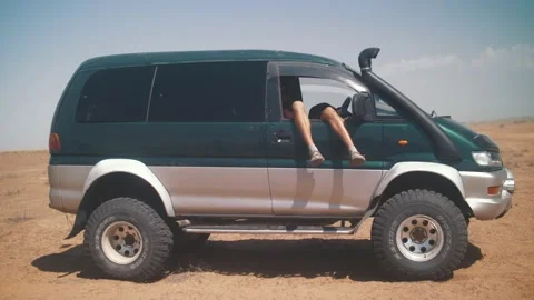 A man is resting with his legs dangling out of the car. Around the desert Stock Footage 221915893