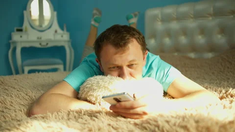 Man is resting lying on a bed in the bedroom with a mobile phone in his hands Stock Footage 131752707