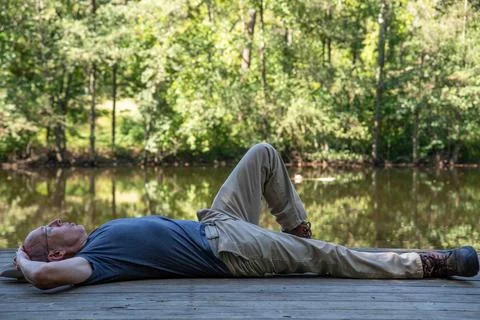 Man resting lying down alone on rustic dock by tranquil woodland pond Stock Photos