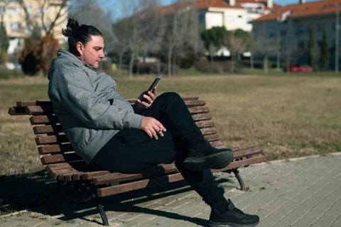 Man resting on park bench using phone outdoors Stock Photos