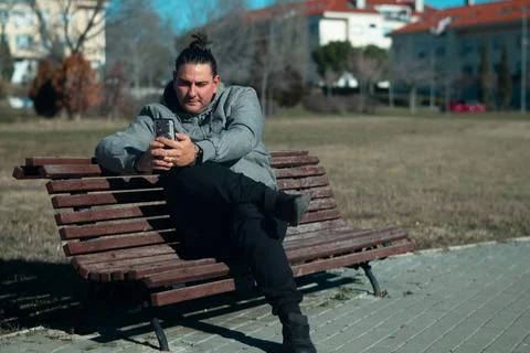 Man resting on park bench using smartphone outdoors Stock Photos