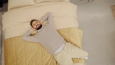 Man resting peacefully on bed, eyes closed and hands behind head, enjoy comfort Stock Footage 334654224