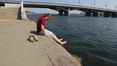 A man is resting by the river, wets his feet Stock Footage 158012198