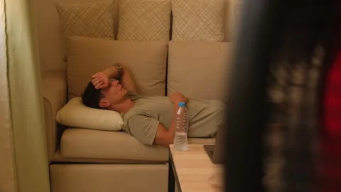 Man resting on sofa during extreme heatwave at home, touching forehead while Stockbeeldmateriaal 346250472