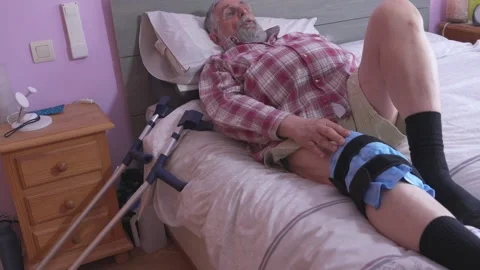 Man rests on a bed, his leg immobilized in a brace - crutches leaning nearby Stock-Footage 335280207