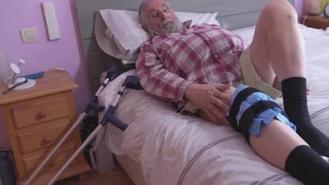 Man rests on bed with leg brace and crutches nearby Stock Footage 335280243