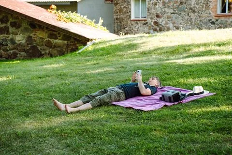 A man rests on a blanket spread on the grass, lying in the park in the summer Stock Photos