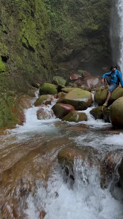 Man Rests on Rocks by Waterfall in Lush Jungle Stream Vertical Stock Footage 321104107
