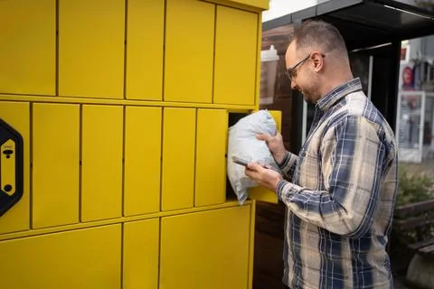 Man retrieving a package from a yellow delivery locker in a busy urban area Stock Photos