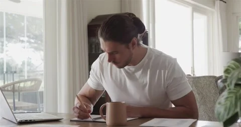 Man reviewing document, jotting notes and typing on laptop while sipping coffee Video stock 317127093