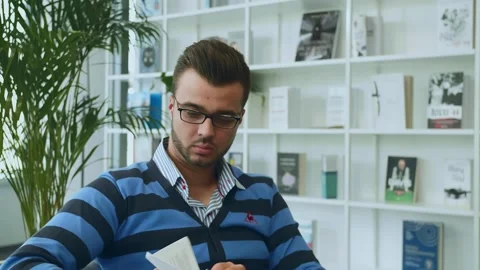 Man Reviewing Documents Sitting in Modern Office with White Shelving Video stock 340265438