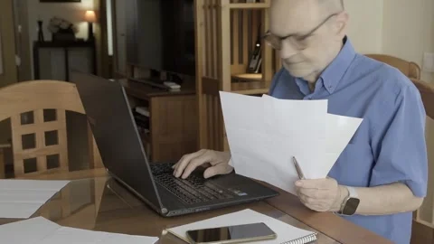 Man Reviewing Documents While Using Laptop at Home Office Stock Footage 309098895