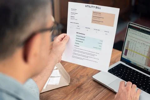 Man reviewing utility bill while working on laptop. Household finance and budget Stock Photos
