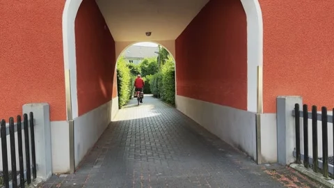 A man rides a bicycle down a brick walkway passage in Germany. The brick walk Vídeos de archivo 347177216