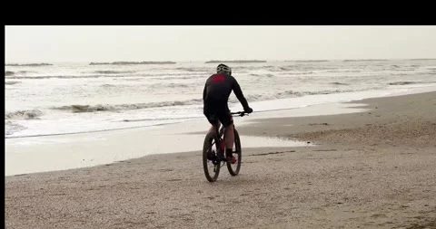 Man rides a bicycle on a sand beach towards waves Stock Footage 270464896