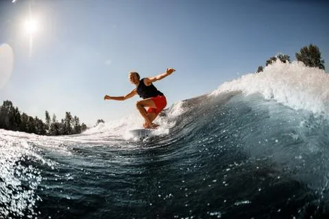 Man rides down the wave on surf style wakeboard on sunny day Stock Photos
