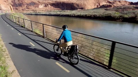 Man Rides E-Bike Along Colorado River and Red Sandstone Cliffs in Moab, Utah Stock Footage 339002788