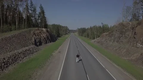 A man rides a longboard on the road between the woods. Stock Footage 149108621