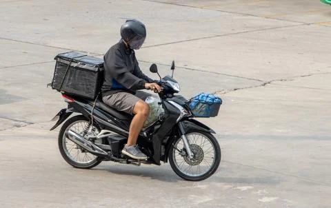 A man rides a motorcycle with a storage box down the street Stock Photos