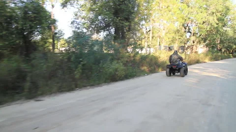 Man rides a quad bike down a road surrounded by trees. Видео 68976831