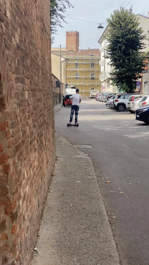 Man riding hoverboard on paved street near brick wall in italian town Stock Footage 291607851
