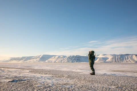 Man with a rifle and binoculars looking out on the arctic landscape at Svalbard Stock Photos
