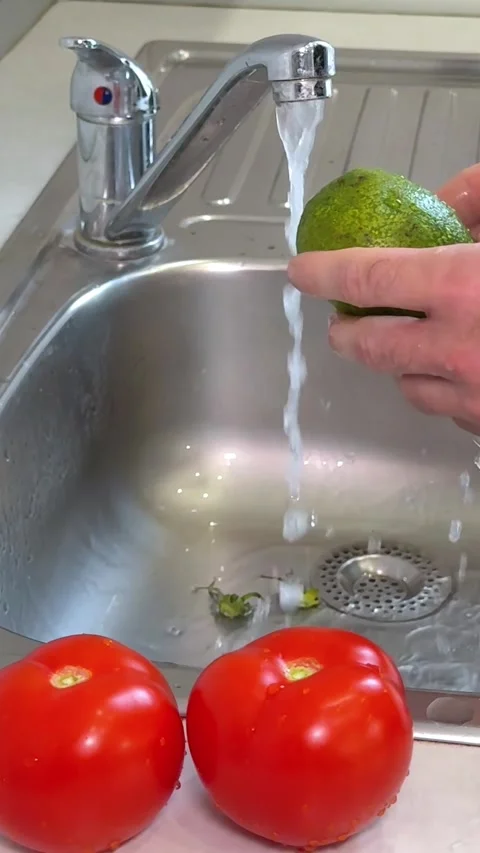 A man rinses a fresh avocado under running water in the kitchen sink, close-up Stock Footage 327563497