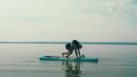 A man rises from his knees on a SUP board in the lake with a paddle 库存影片 218200895