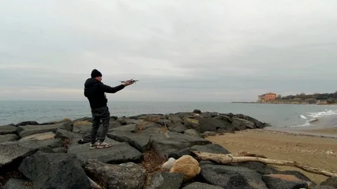 A man on a rock beach do an hand takeoff with a drone 2 Stock Footage 86053672