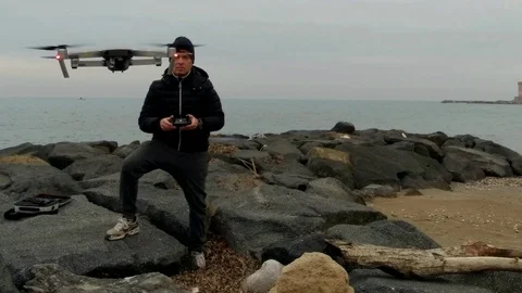 A man on a rock beach do an hand landing with a drone 1 Stock Footage 86053724
