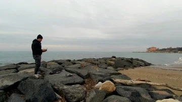 A man on a rock beach do a takeoff with a drone Stock Footage 86053673