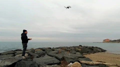 A man on a rock beach drive a drone over the sea Stock Footage 86053737