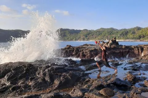 A man on a rock short time before getting wet from a big wave Foto stock