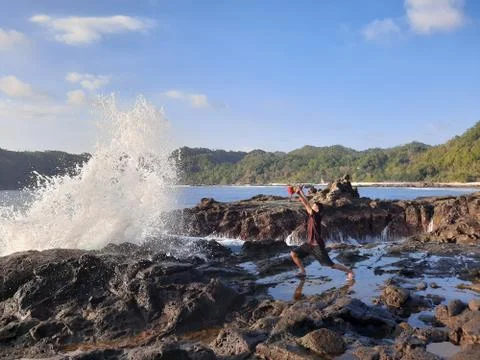 A man on a rock short time before getting wet from a big wave Stock Photos