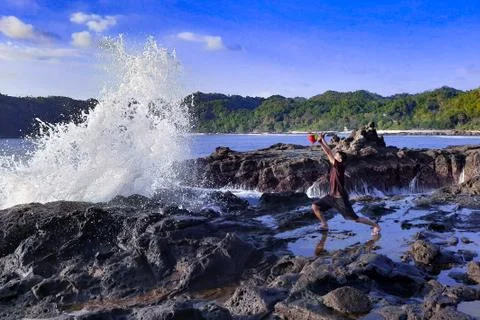 A man on a rock short time before getting wet from a big wave Foto stock