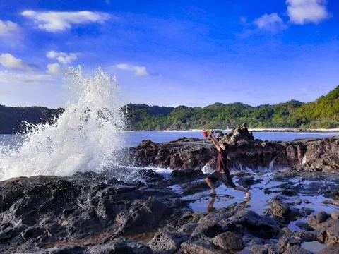 A man on a rock short time before getting wet from a big wave Stock Photos